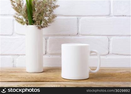 White coffee mug mockup with grass and green leaves in cylinder . White coffee mug mockup with meadow grass and green leaves in cylinder vase near painted brick wall. Empty mug mock up for design promotion.