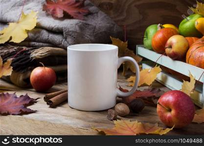 White coffee mug mockup with knitted plaid, maple fall leaves and apples. Empty mug mock up for design promotion.