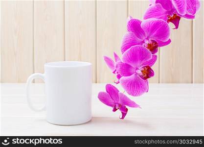 White coffee mug mockup with pink orchid. White coffee mug mockup with pink orchid. White coffee cup mock-up for brand promotion. Empty mug mockup for design presentation.