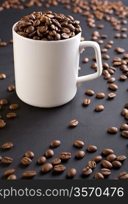 white coffee mug with coffee grains on a black background with coffee grains