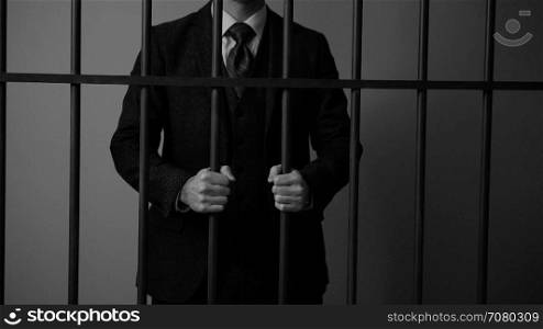 White collar criminal grips bars in a prison cell