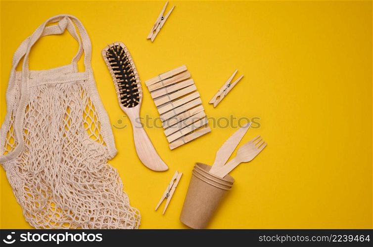 white cotton bag, paper cups and wooden forks and spoons on a yellow background. Recyclable waste, top view