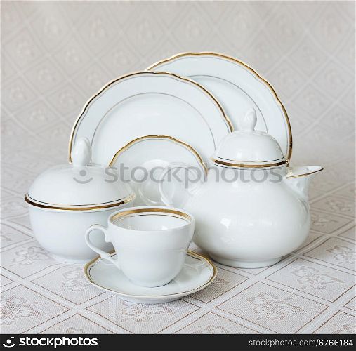 White crockery for tea: teapot, cup, serving plate and sugar bowl on a beautiful tablecloths