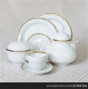 White crockery for tea: teapot, cup, serving plate and sugar bowl on a beautiful tablecloths