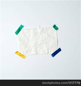 white crumpled sheet of paper torn from a spiral notebook and glued with multi-colored electrical tape on a white background, place for text