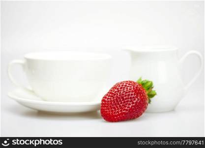 white cup and milk jug with strawberries isolated on white