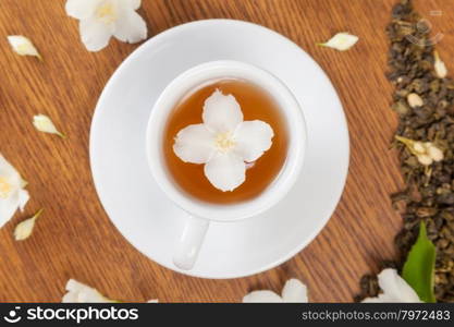 white cup and saucer with jasmine flowers on a wooden table. view from above