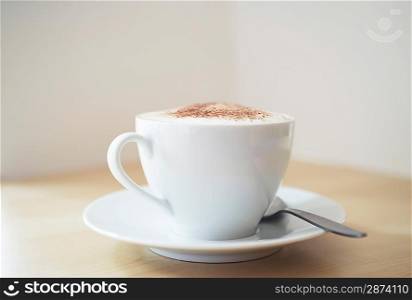 White cup of cappuccino on wooden table close-up
