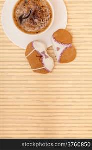 White cup of coffe with funny bikini underwear shape gingerbread cake cookie sweet dessert with white icing and violet decoration border or frame on beige bamboo mat background