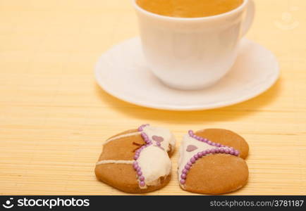 White cup of coffe with funny bikini underwear shape gingerbread cake cookie sweet dessert with white icing and violet decoration on beige bamboo mat