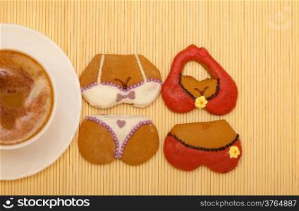 White cup of coffe with funny bikini underwear shape gingerbread cakes cookies sweet dessert with icing and decoration on beige bamboo mat