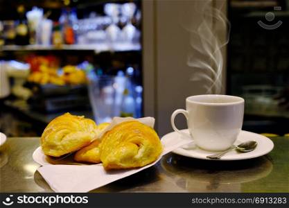 White cup of coffee and croissant over blurred cafe interior