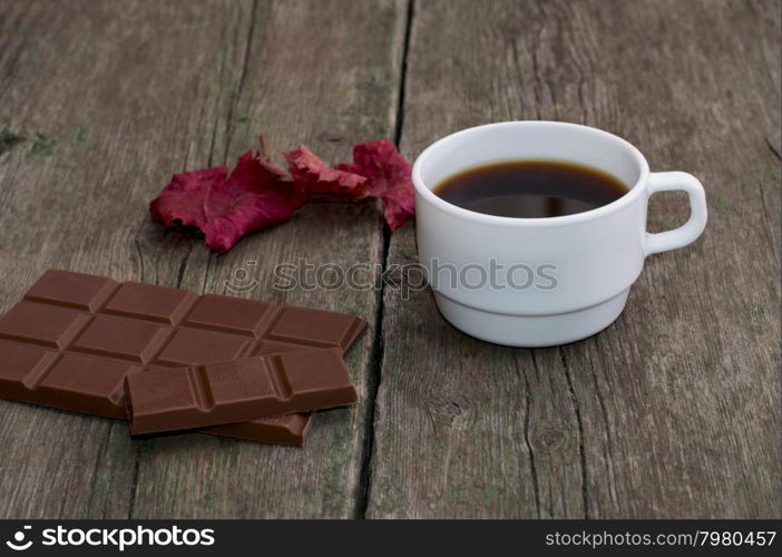 white cup of coffee, chocolate and red leaf, on a wooden table, a still life a subject drinks