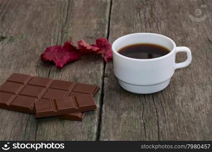 white cup of coffee, chocolate and red leaf, on a wooden table, a still life a subject drinks