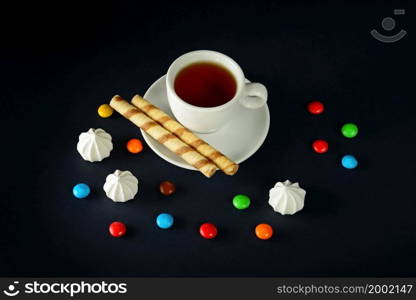 White cup of coffee , multi-colored sweet drops and meringues on a black background.