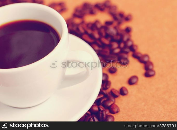 White cup of coffee on coffee beans with retro filter effect