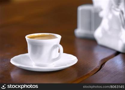 White cup of coffee on wooden table with blurred background. White cup of coffee on wooden table