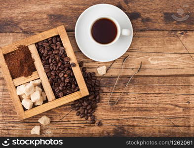 White cup of fresh raw organic coffee with beans and ground powder with cane sugar in vintage box on wooden background.