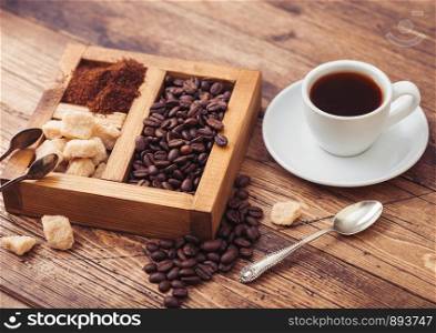 White cup of fresh raw organic coffee with beans and ground powder with cane sugar in vintage box on wooden background.