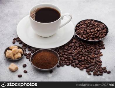 White cup of fresh raw organic coffee with beans and ground powder with cane sugar cubes with coffee tree leaf on light background. Top view