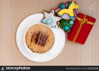 White cup of hot beverage drink coffee cappuccino latte with christmas handmade gingerbread cakes with icing sweet dessert and red gift box with golden ribbon. Holiday concept.