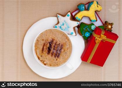 White cup of hot beverage drink coffee cappuccino latte with christmas handmade gingerbread cakes with icing sweet dessert and red gift box with golden ribbon. Holiday concept.