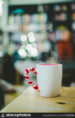 White cup of tea is standing on a wooden table. Steam and blurry background whit lights.
