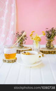 White cup of tea with linden in natural organic herbs and a jar of honey on a white wooden table. Increase immunity in the cool season.. White cup of tea with linden in natural organic herbs and a jar of honey on a white wooden table.