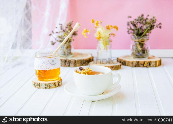 White cup of tea with linden in natural organic herbs and a jar of honey on a white wooden table. Increase immunity in the cool season.. White cup of tea with linden in natural organic herbs and a jar of honey on a white wooden table.