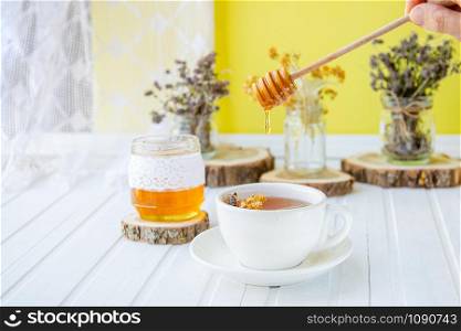 White cup of tea with linden in natural organic herbs and a jar of honey on a white wooden table. Increase immunity in the cool season.. White cup of tea with linden in natural organic herbs and a jar of honey on a white wooden table.