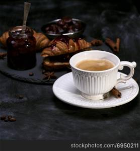 white cup with black coffee on the table, behind croissant with jam