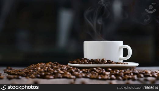 White cup with espresso coffee and grains on a wooden dark table, steam over coffee, copy space for text, close-up