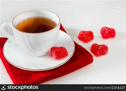White cup with tea on a red napkin and heart shaped marmalade on a white background. Symbol of love, valentines day, gift card. White cup with tea on a red napkin