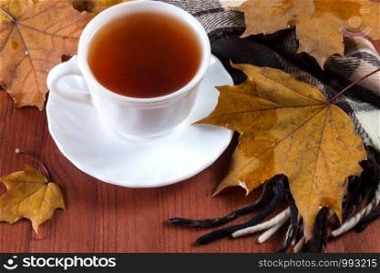 White cups with tea and scarf on wooden background with autumn leaves. Cup with tea on the table with autumn leaves
