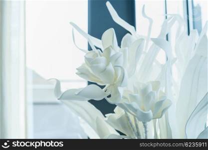 White decoration artificial flowers at window background, close up