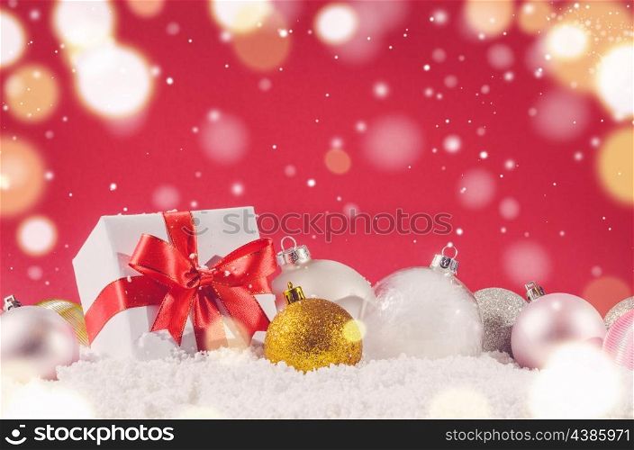 white decorative christmas gift box with ribbon and balls on snow against red festive background. christmas gift box and balls