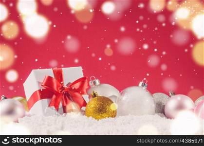 white decorative christmas gift box with ribbon and balls on snow against red festive background. christmas gift box and balls