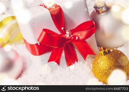 white decorative christmas gift box with ribbon and balls on snow, view from above
