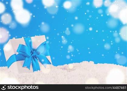 white decorative christmas gift box with ribbon on snow against blue festive background. christmas gift box