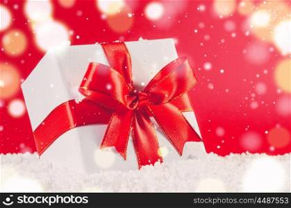 white decorative christmas gift box with ribbon on snow against red festive background. christmas gift box