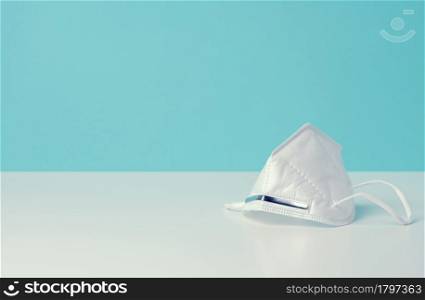 white disposable medical mask on a blue background, personal protective equipment for the respiratory tract from viral infections, copy space