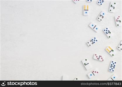 White dominoes with colorful dots lie to the right on a white cement background with copy space on the left ,flat lay close-up.Summer board game concept.. White dominoes with colorful dots on a white cement background, top view. Board game.