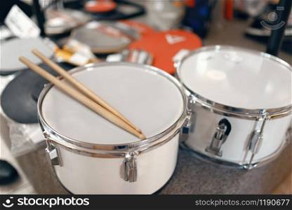 White drums and drumsticks on showcase in music store, closeup view, nobody. Assortment in musical instrument shop, professional equipment for musicians and performers