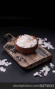 White dry coconut flakes in a wooden bowl prepared for making desserts on a textured concrete background