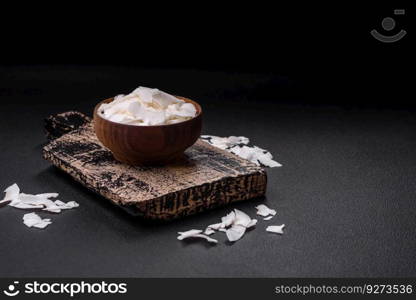 White dry coconut flakes in a wooden bowl prepared for making desserts on a textured concrete background