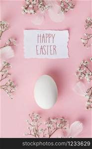 White Easter egg and flowers on pastel pink background. Happy Easter concept. Space for text