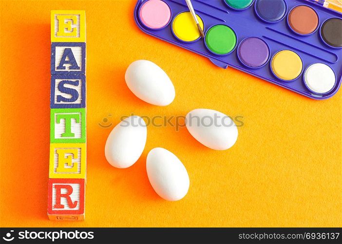White easter eggs and paint displayed against an orange background with the word easter
