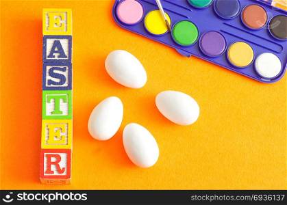 White easter eggs and paint displayed against an orange background with the word easter