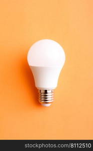 White economy light bulb on orange background.