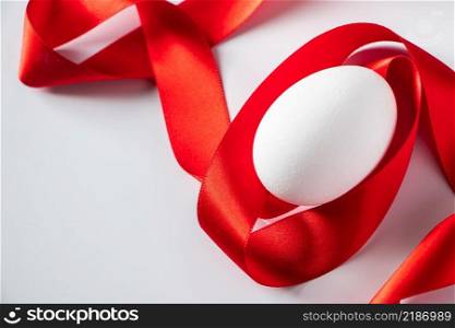 White egg with red silk ribbon. Easter symbol. Closeup white egg with red silk ribbon, easter symbol on a light background. Place for text.. White egg with red silk ribbon. Easter symbol.